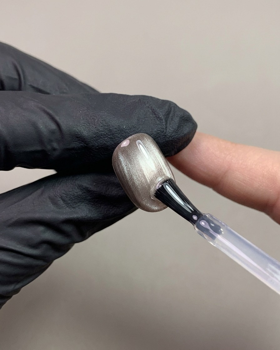 A nail brush applying a clear non-wipe top coat over a dark brown magnetic cat-eye nail.