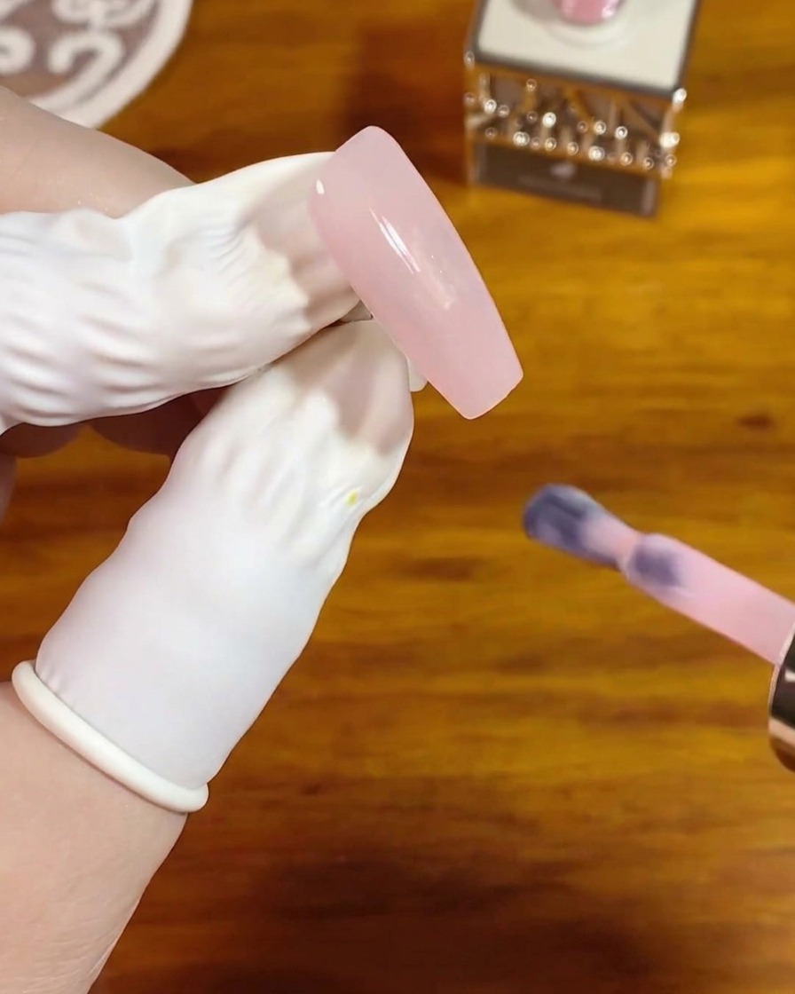 A nail brush applying a smooth coat of translucent pink crystal gel to a bare, long square nail.