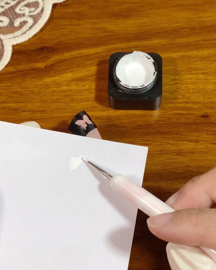 A dotting tool placing a small dollop of thick white patting gel onto a white palette paper.