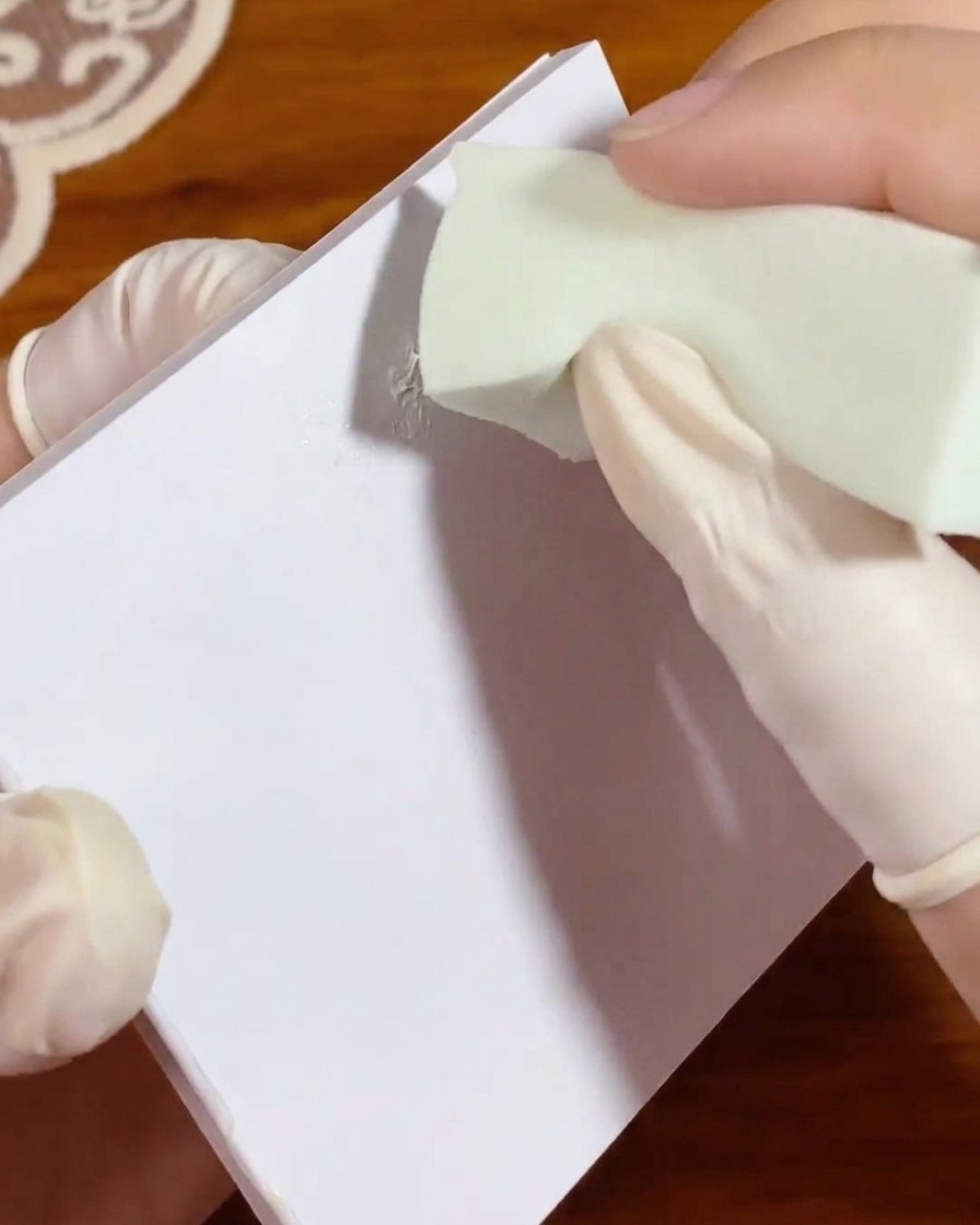 A small green makeup sponge being dabbed into a patch of white gel on a palette paper to evenly distribute the color.