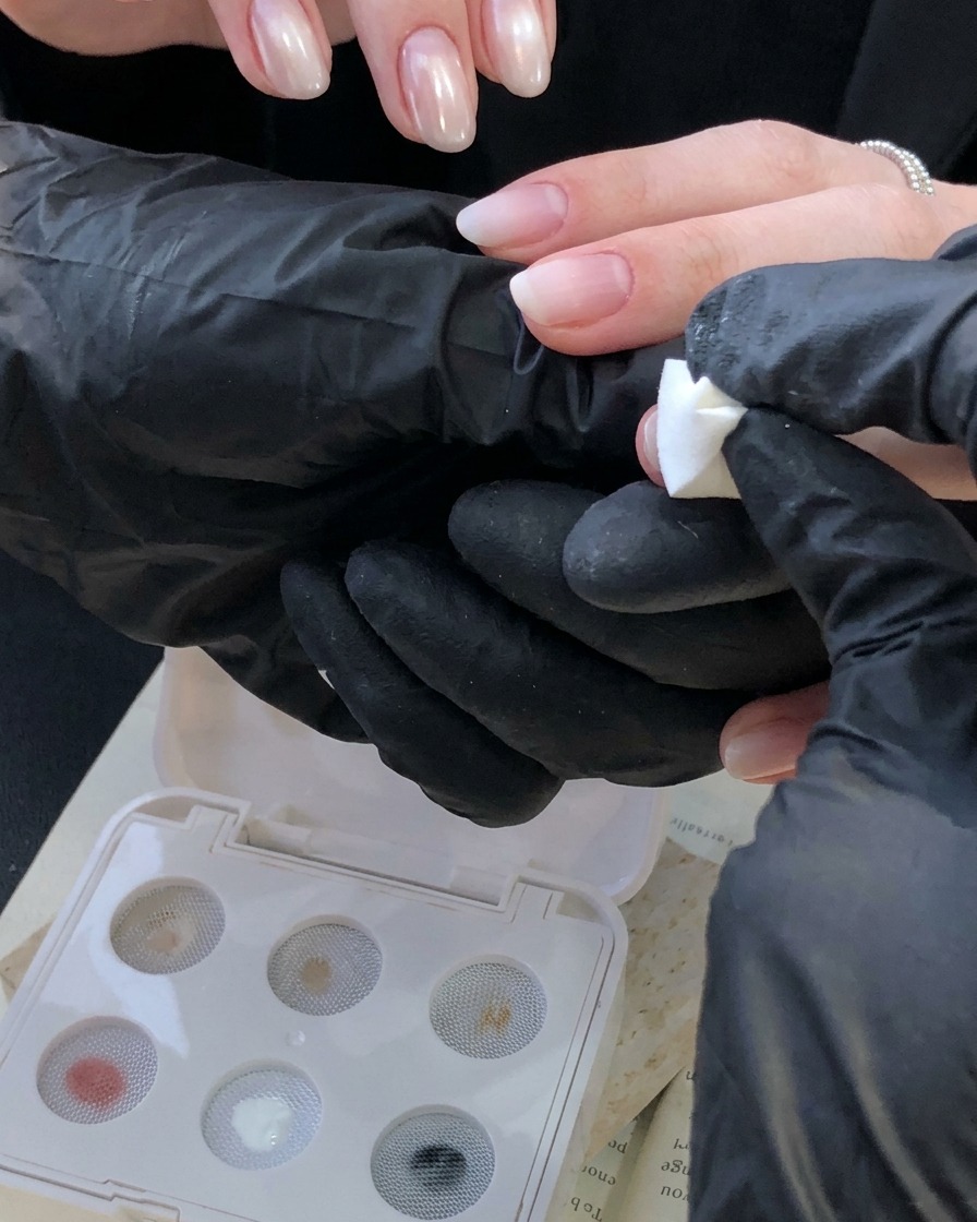 A gloved hand using a white sponge stamp tool to apply an ivory white gradient onto a fingernail near the cuticle.