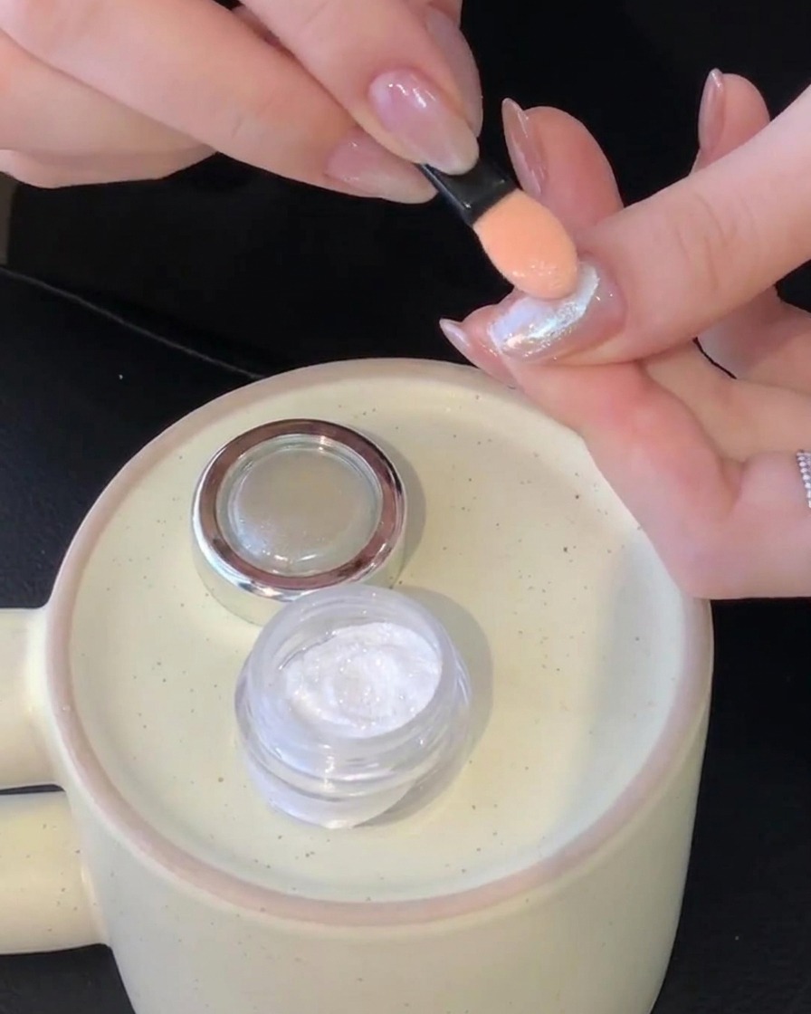 A sponge applicator buffing white aurora chrome powder onto a cured nail surface.