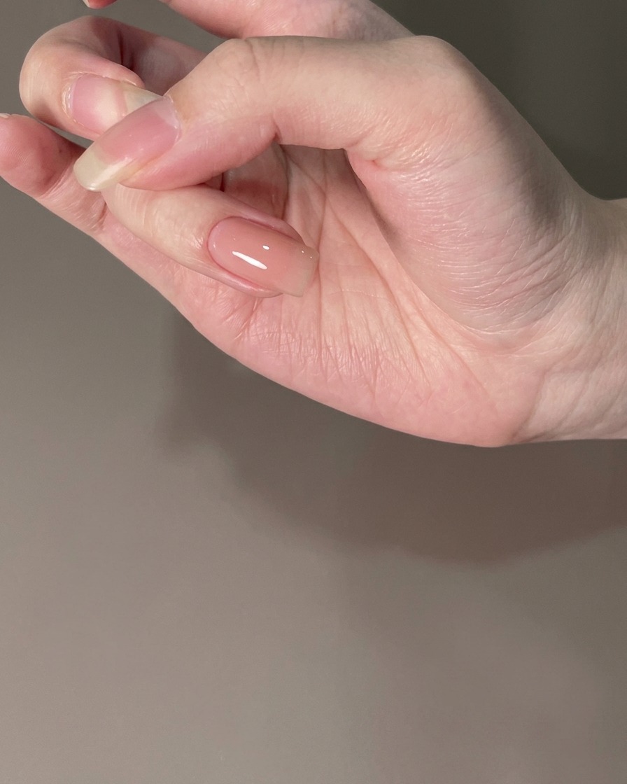 A fingernail with a cured nude base coat under lighting.