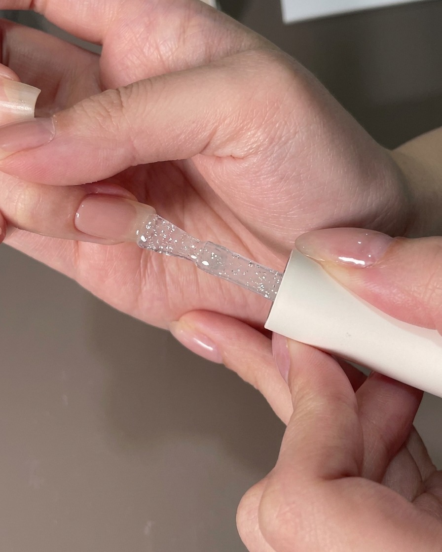 A flat brush smoothing a clear gel layer over a fingernail to remove particles.