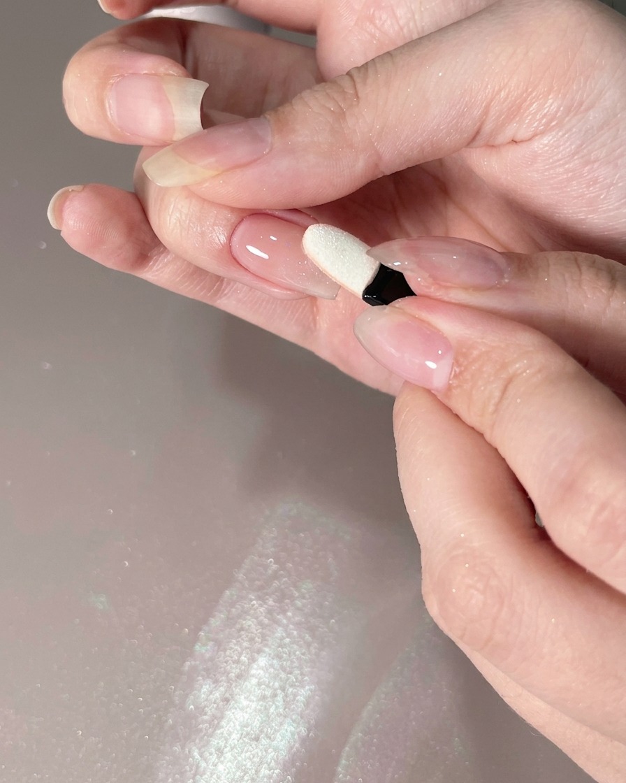 A sponge applicator applying chrome powder onto the tip of a nail.