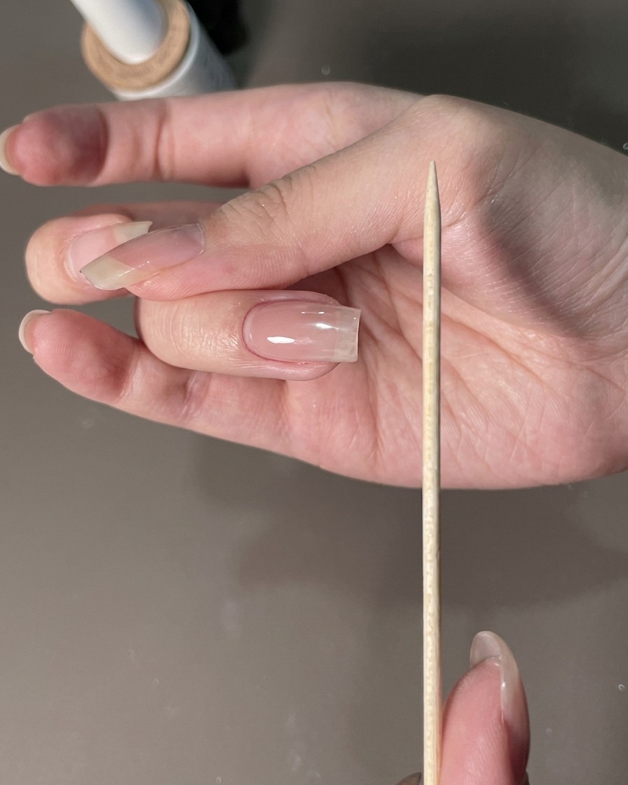 A nail file held next to a manicured hand to shape the nail edges.