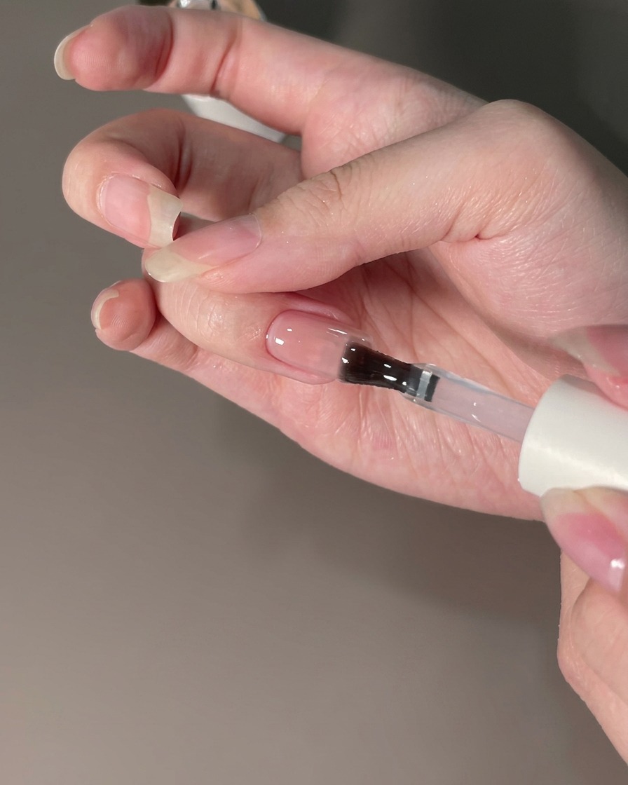 A brush applying a top coat sealant over a chrome powder-finished nail.