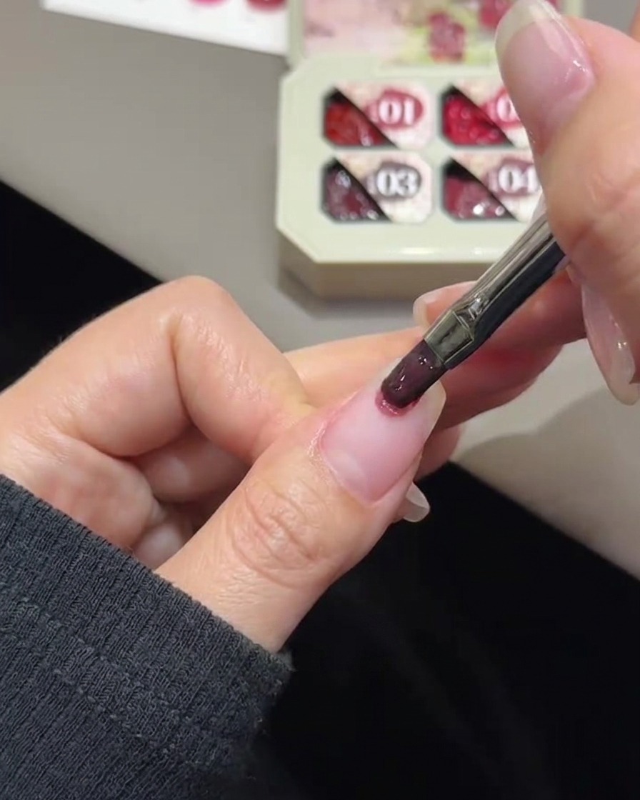 A nail brush dabbing rose color gel onto the tip of a natural fingernail.