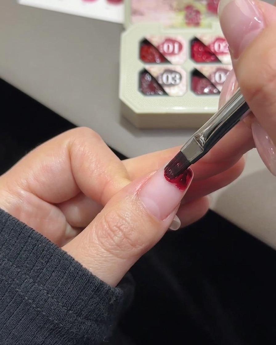 A small white makeup sponge wedge blending rose gel color on a fingernail tip.
