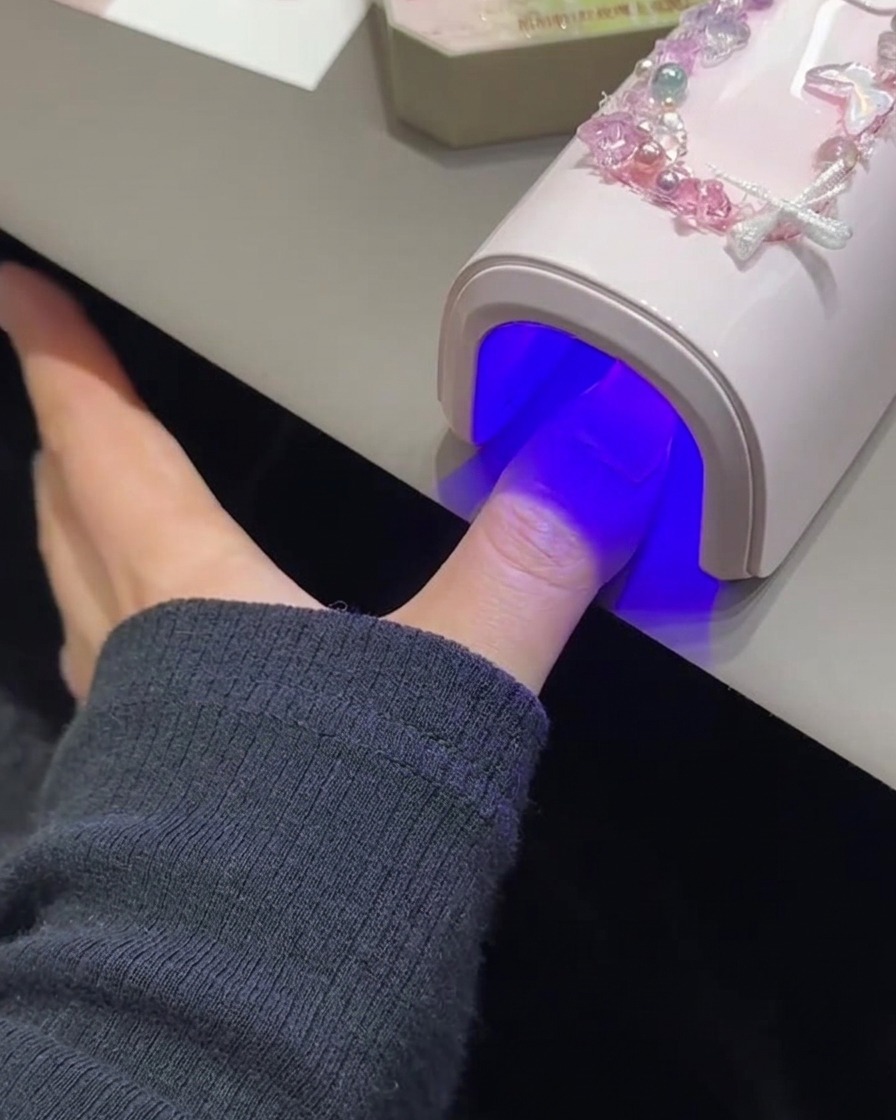 A fingernail curing under a pink UV/LED lamp.