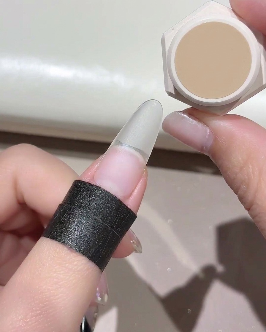 A small sponge dabbing a nude gel color onto a clear false nail extension.