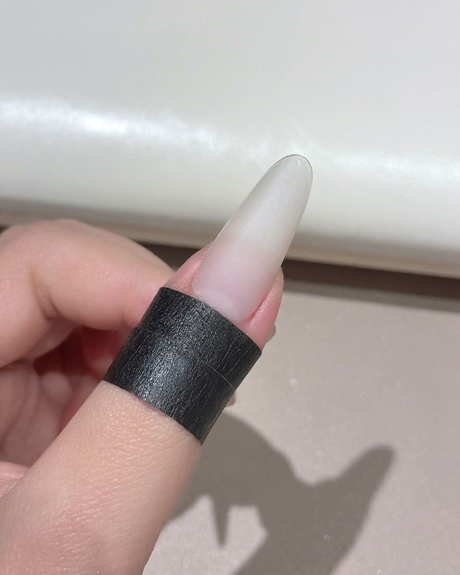 A manicured nail positioned underneath a compact handheld UV LED lamp.