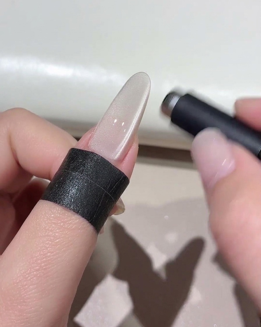 A cylindrical magnet hovering over a shimmering cat-eye nail to shape the light effect.