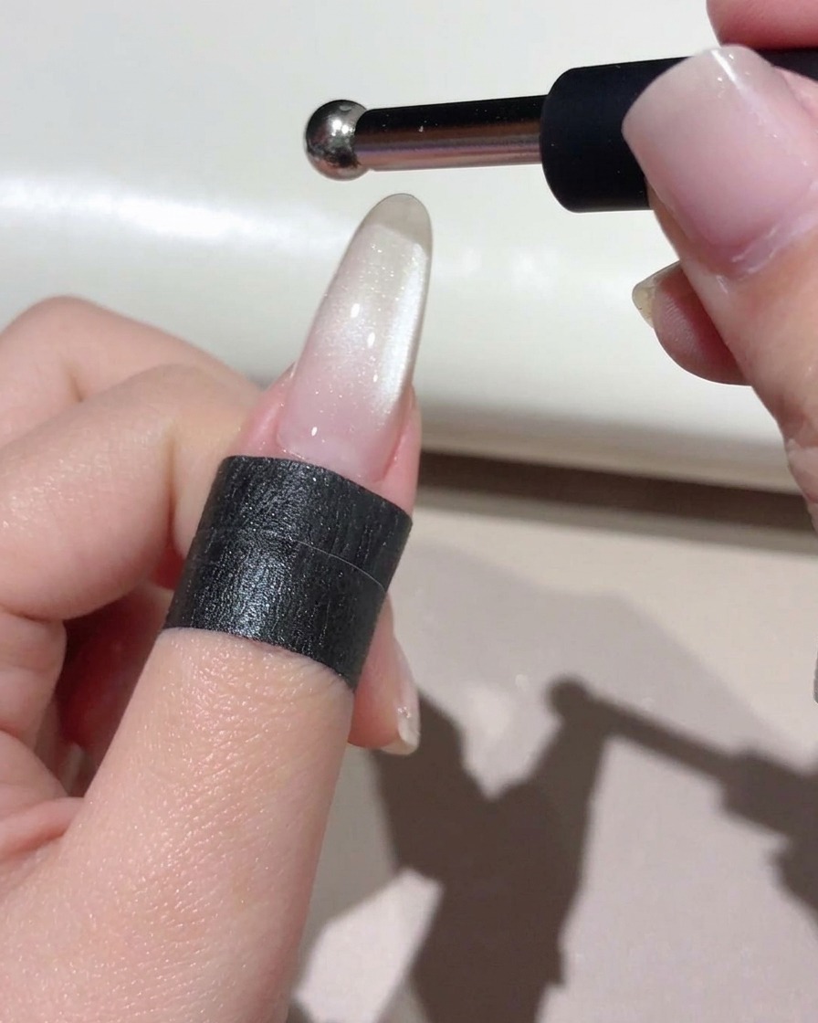 A small ball-point magnet held above the nail to shape a concentrated glass bead reflection.