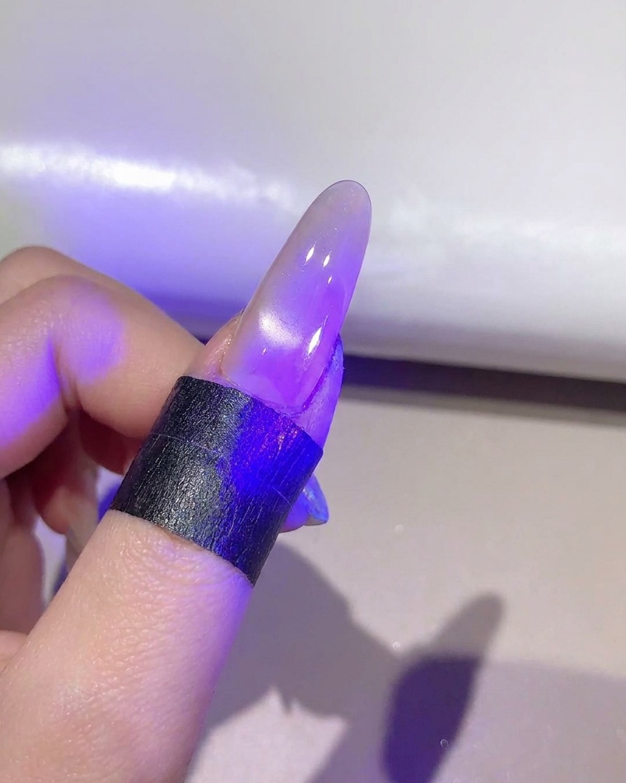 A nail under a purple UV/LED lamp curing the finished cat-eye gel layer.
