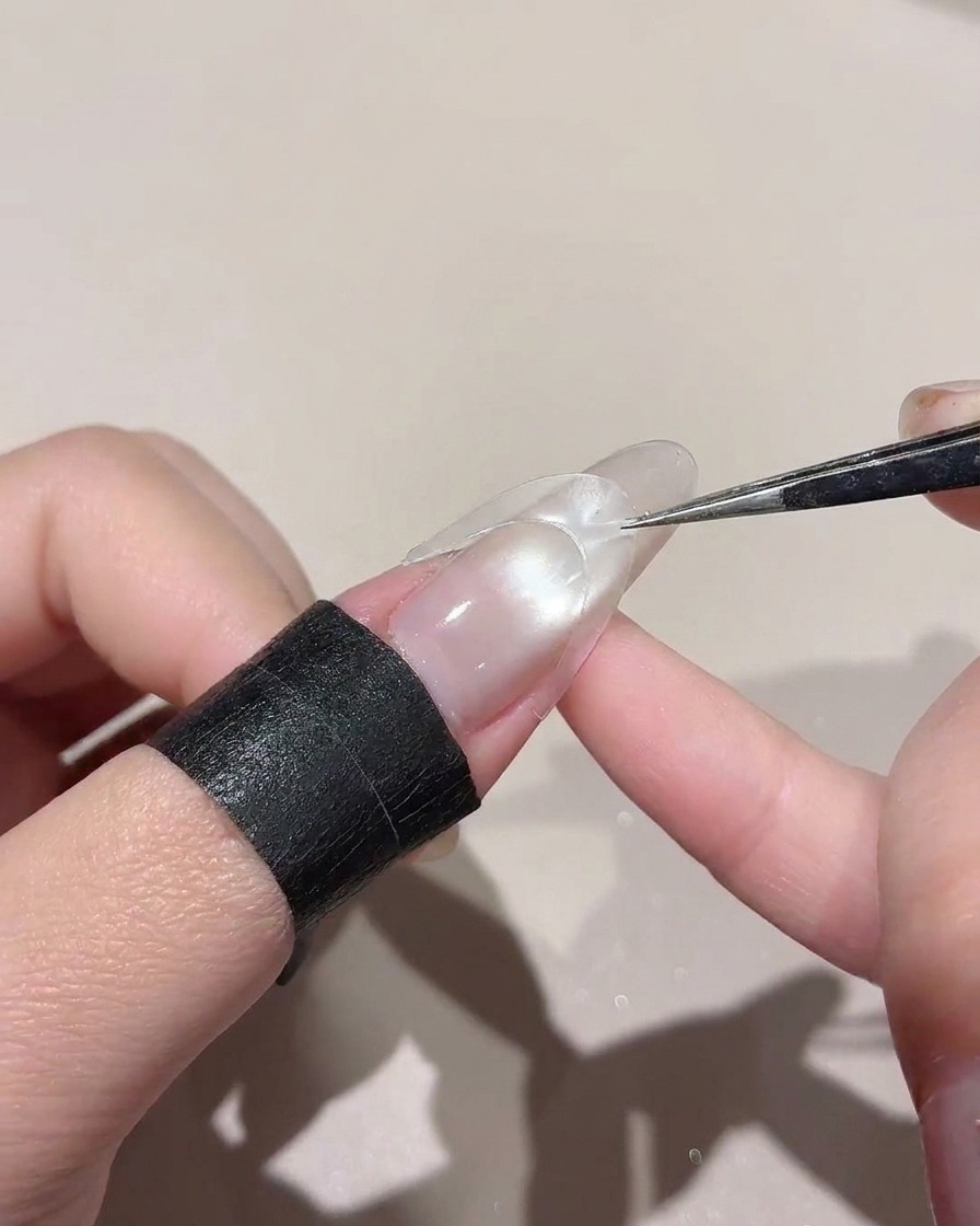 A curved sticker being placed across the middle of a glossy nail using tweezers.