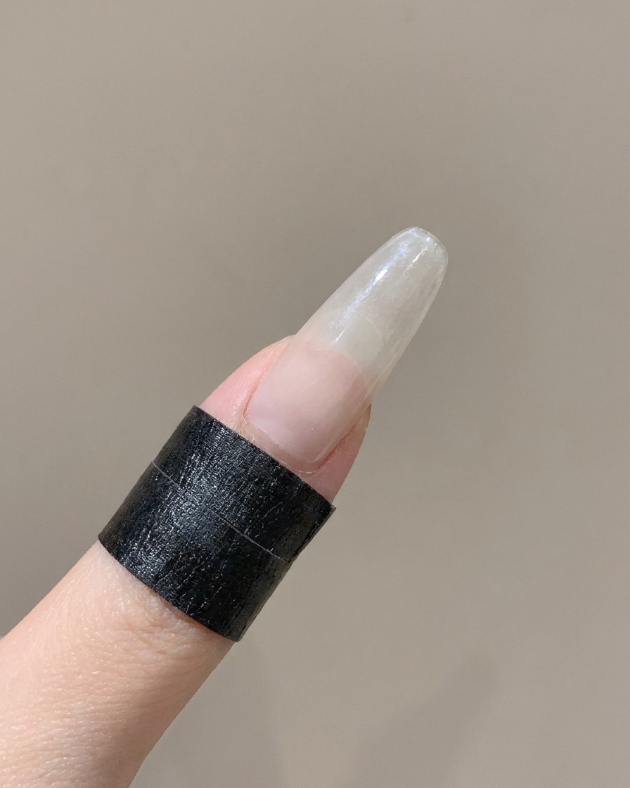 A silicone tool pressing down the curved edge of a French nail sticker on a finger.
