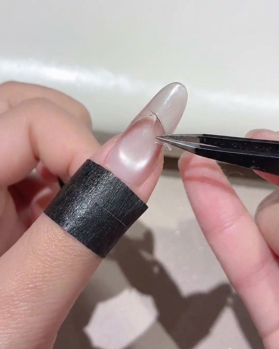 Tweezers pulling a curved sticker off a nail to expose a sharp gradient line.