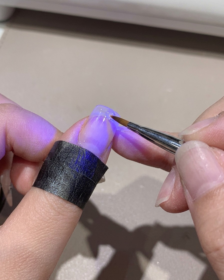 A mini UV lamp curing a gradient nail tip while held by hand.