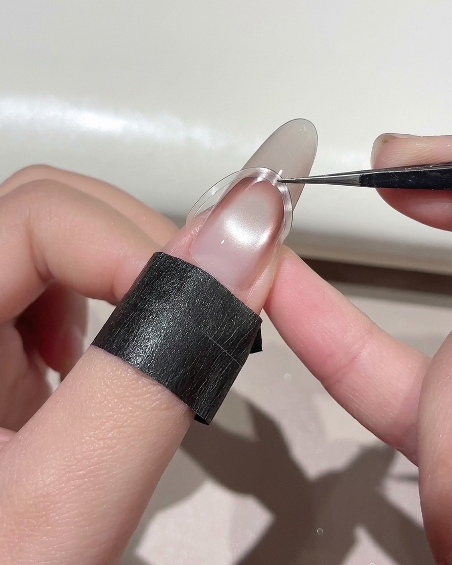 Tweezers placing a curved French nail sticker slightly higher on a manicured nail.
