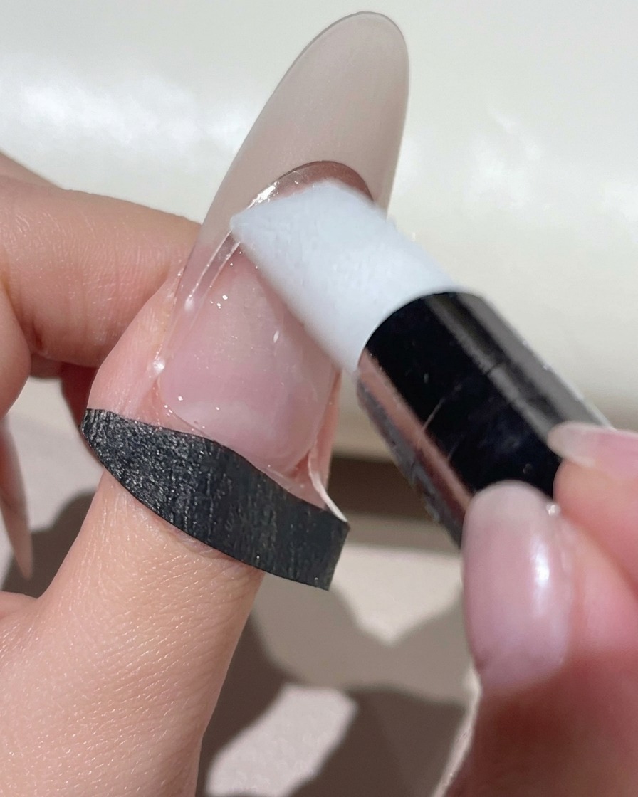 A white silicone makeup tool pressing down a curved French guide sticker on a natural-toned nail.