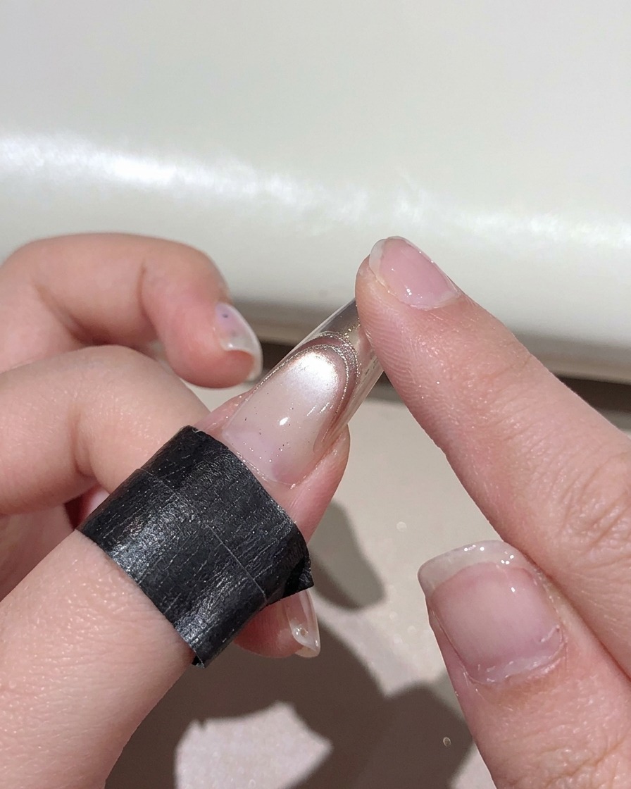 A finger rubbing rose gold metallic powder onto the tip of a manicured nail.