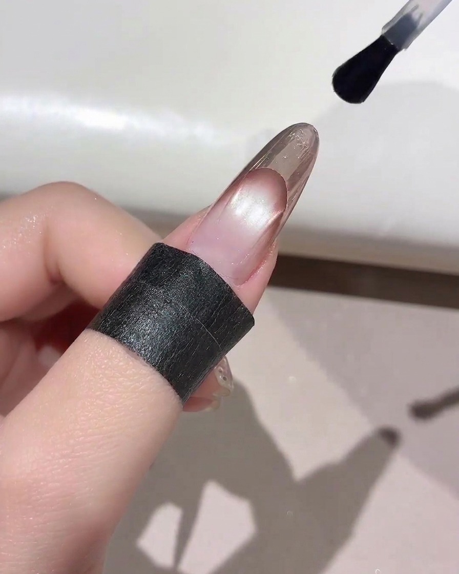 A nail brush applying a clear top coat over the tip of a finished French manicure.