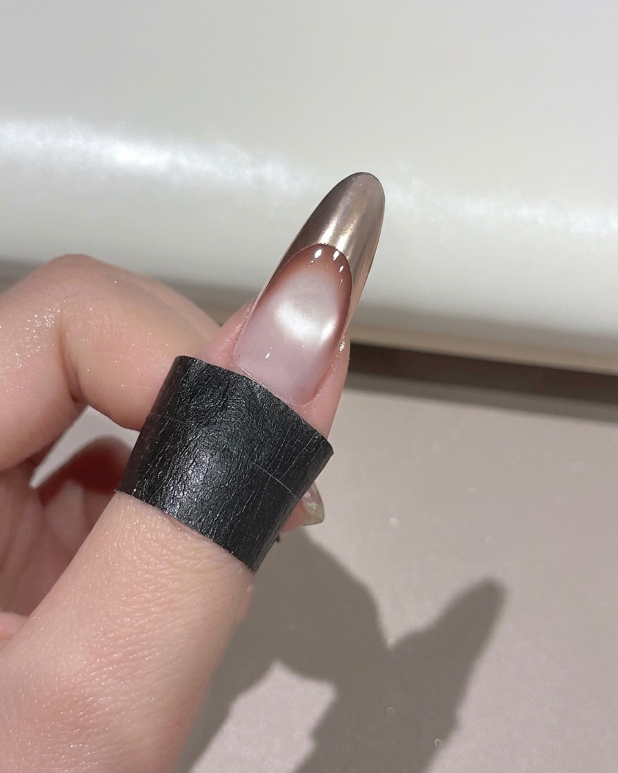 A finger with a gold chrome French tip resting inside a UV nail lamp for curing.