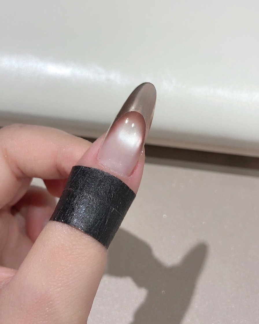 A nail brush applying a clear glossy top coat over a finished gold rose French manicure.