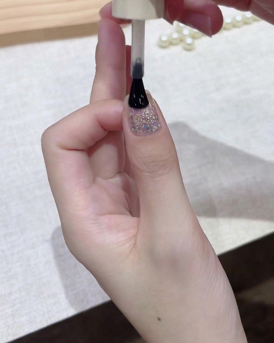 A polish brush applying a thin layer of dark gel polish across the surface of the nail.