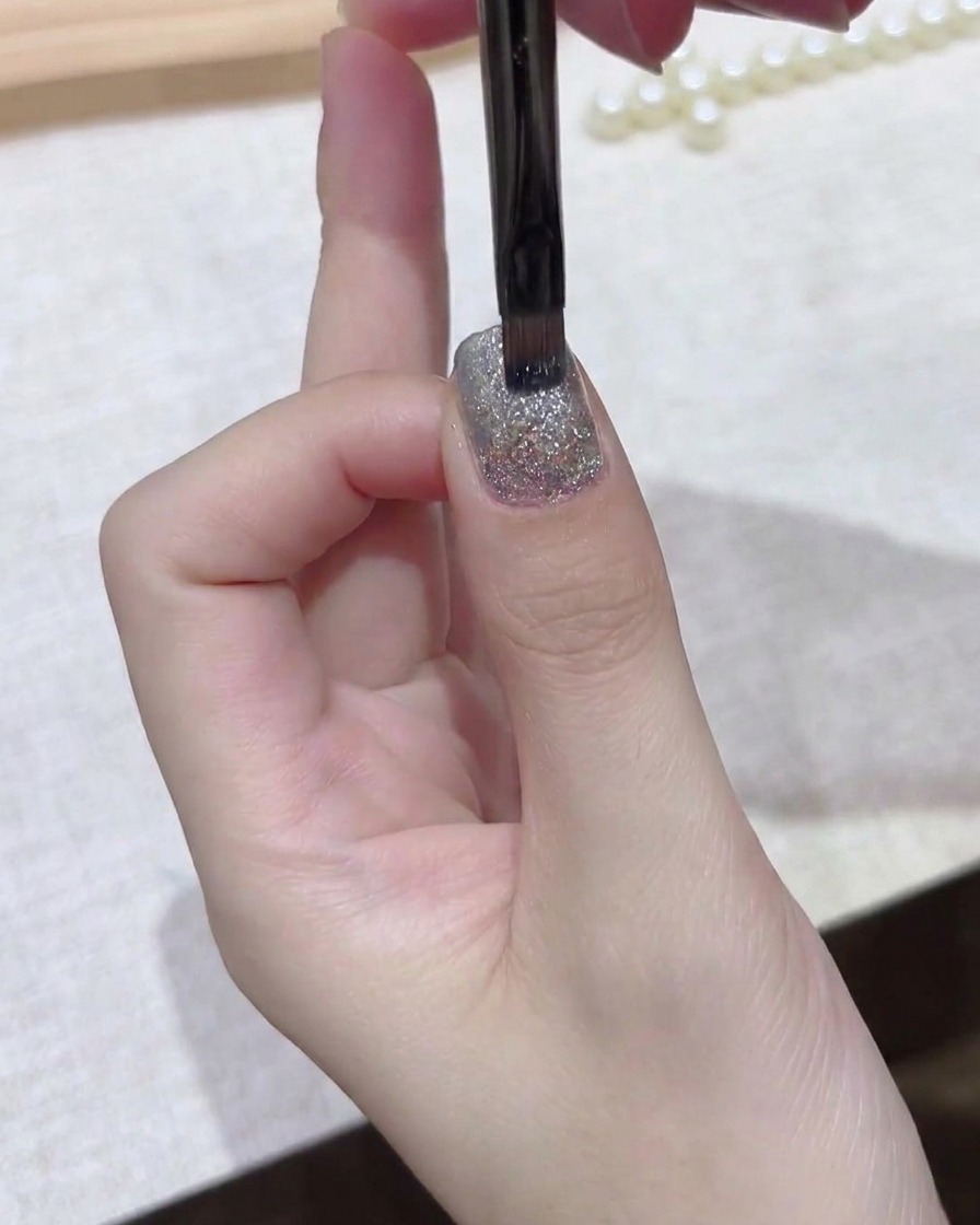 A fine brush smoothing out a dark gel layer evenly across the nail plate.