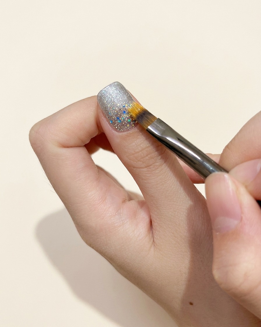 A cleanup brush refining the edges of a gel application near the cuticle of a fingernail.
