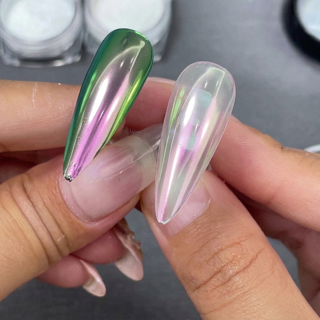 Two finished stiletto nail tips held side-by-side, one with a clear base and one with a black base showing a green-purple shift.