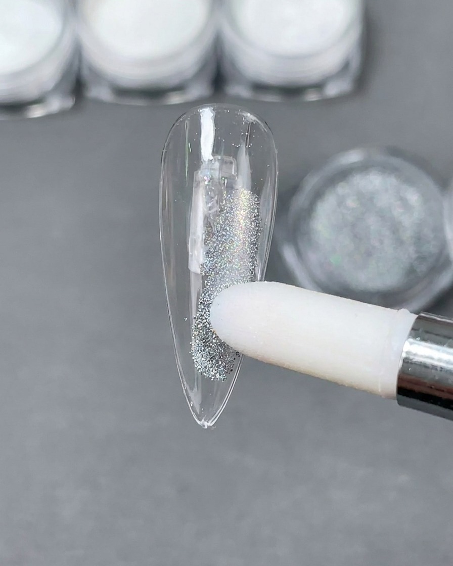 A sponge applicator placing silver Laser holographic powder onto a clear stiletto nail tip.
