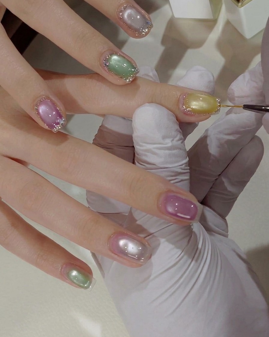 A close-up view of small, colorful butterfly flakes being placed onto a decorated nail surface with a fine tool.