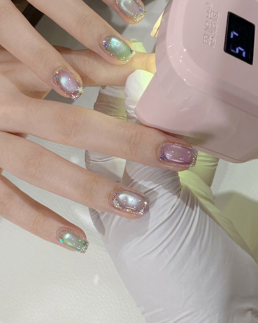 A close-up shot of a clients hand positioned under a pink mini UV/LED nail lamp for curing.