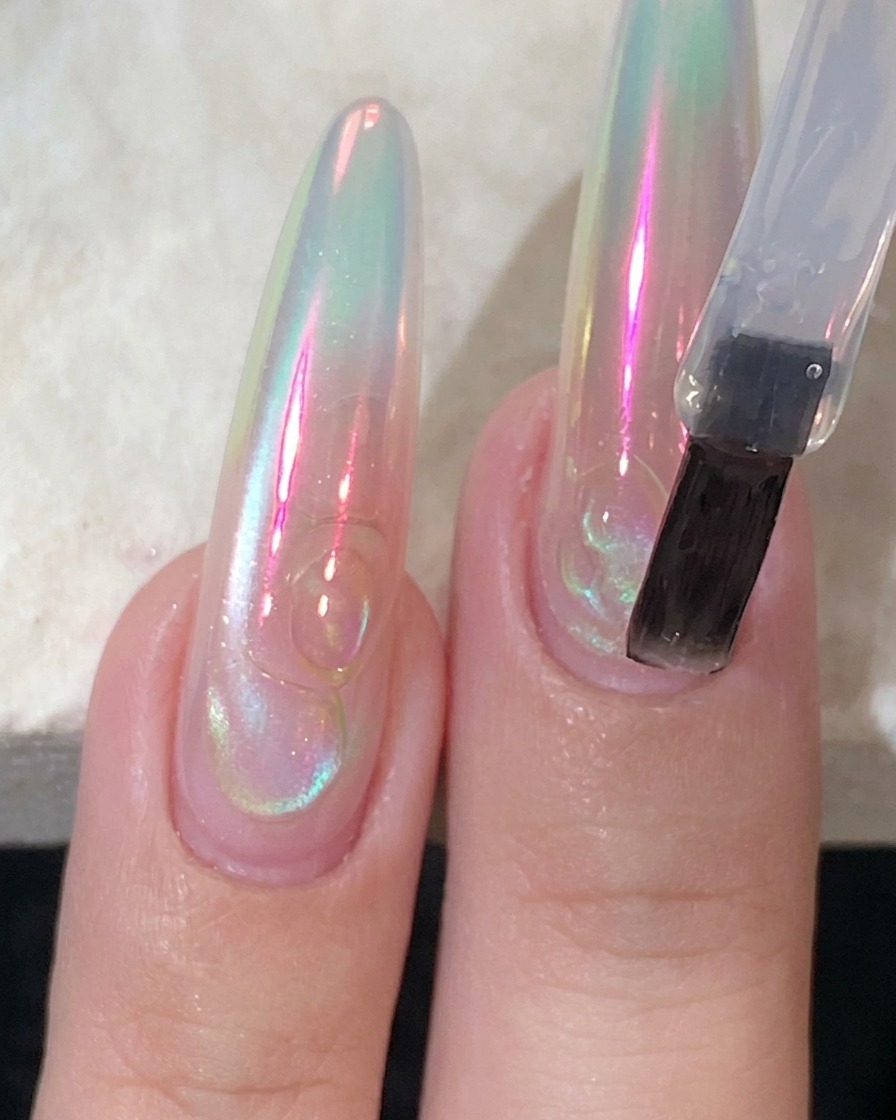 A flat nail brush applying a clear, glossy top coat onto a long extension nail.