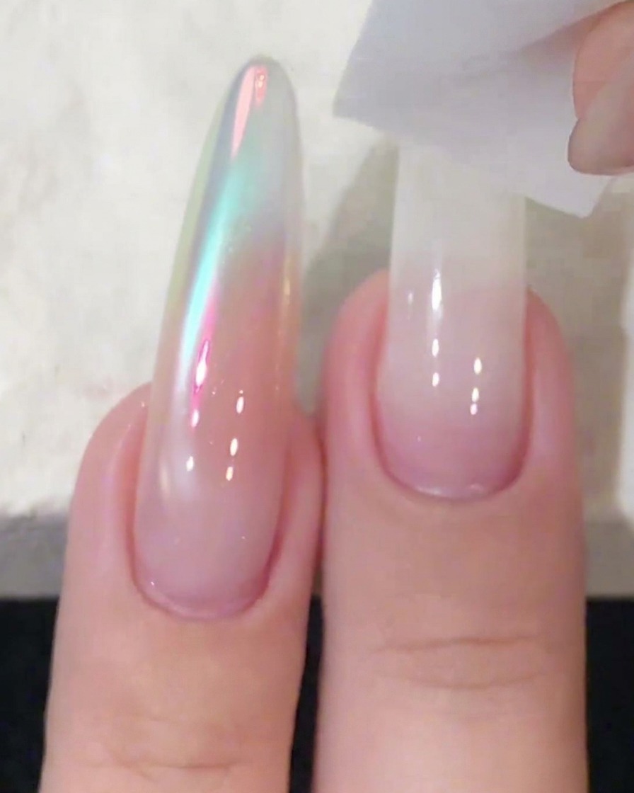 A sponge block being used to pat and blend white gel polish on a long nail extension.