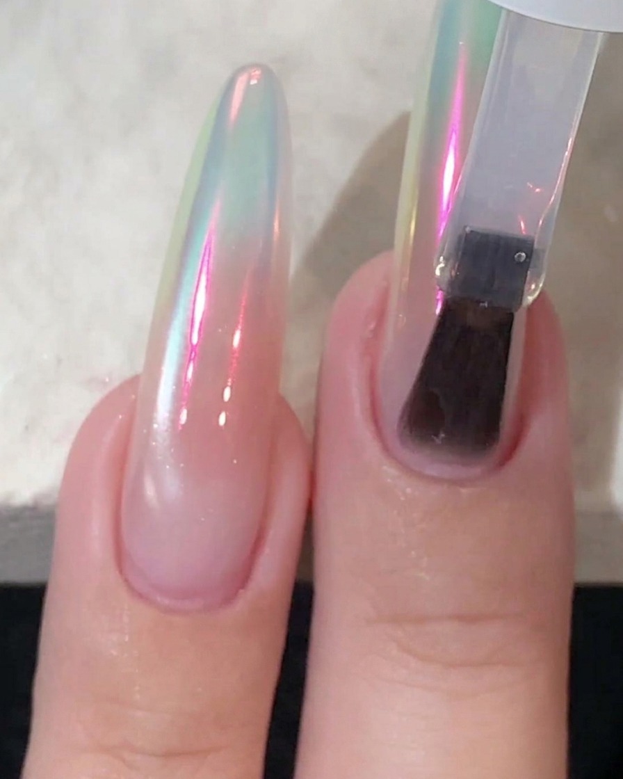 A sponge applicator buffing chrome powder onto a glossy nail until it reflects an aurora sheen.