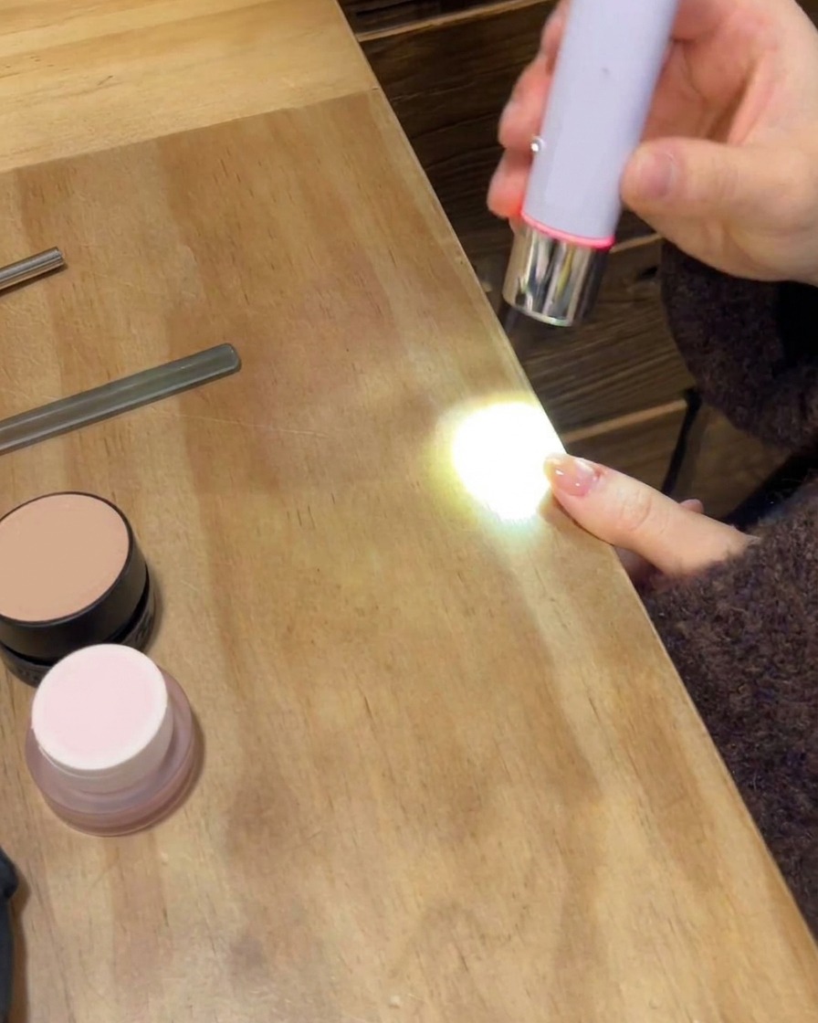 A portable UV/LED lamp curing the final glossy top coat on a manicured hand.