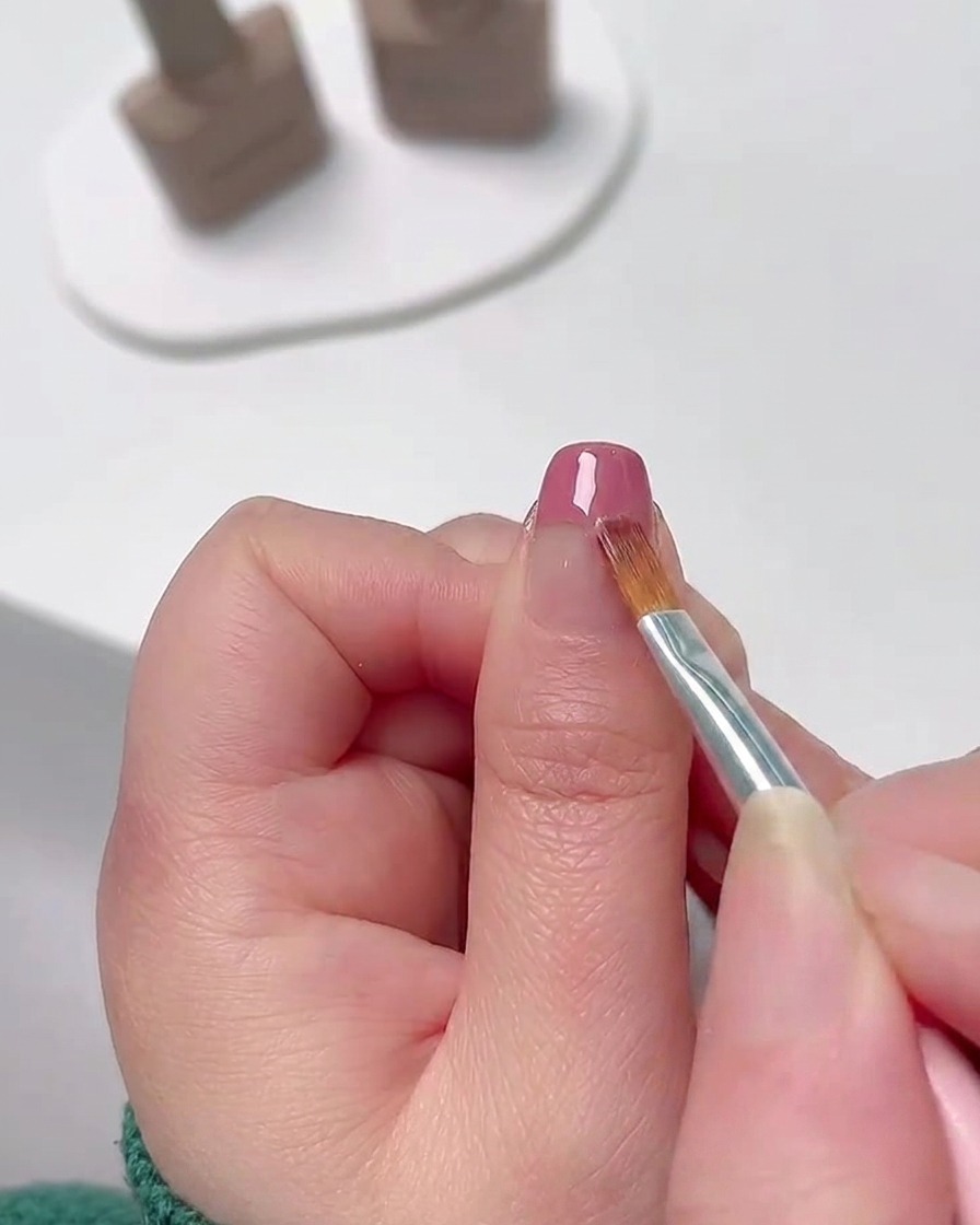 A close-up of a fine nail art brush blending pink gel polish down from the tip of the nail to create a soft color gradient.