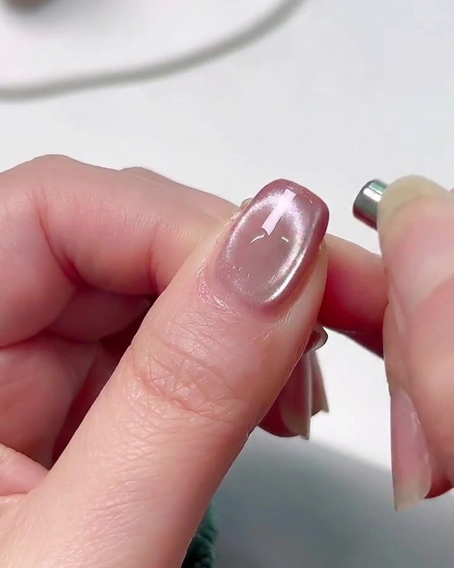 A hand placed inside a professional UV nail curing lamp with a soft pink glow illuminating the fingers.