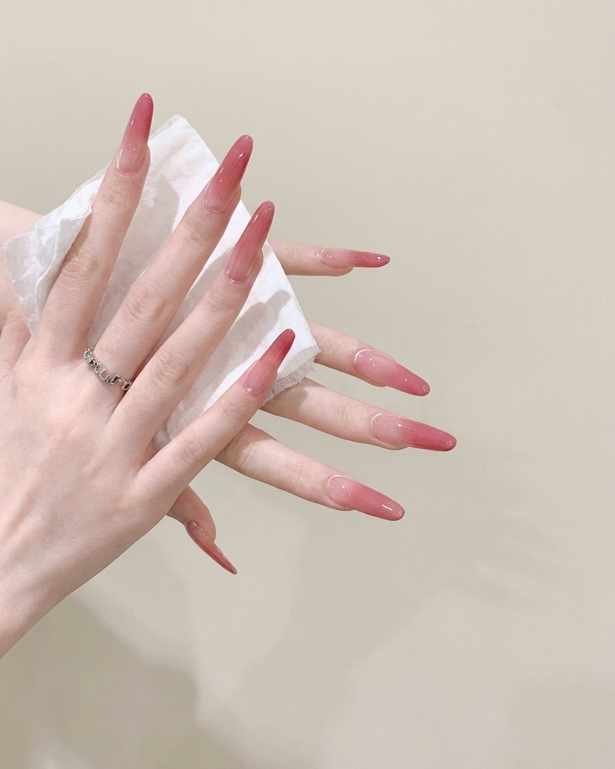 A close-up view of a pair of hands wiping clean long stiletto nails with a wet white tissue.