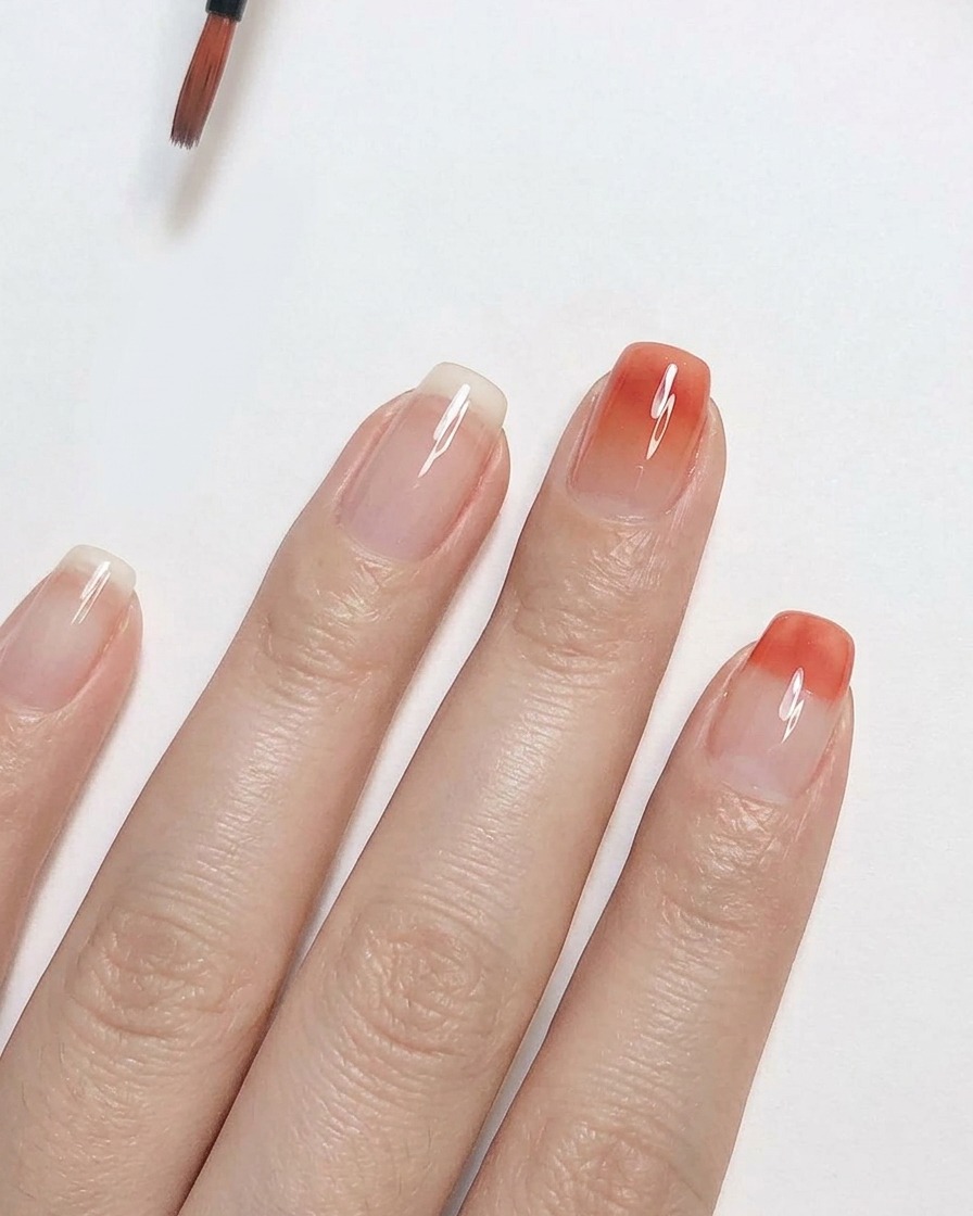 A fine detailing brush blending peach pink gel polish upward on a clear nail to create a smooth ombre gradient effect.