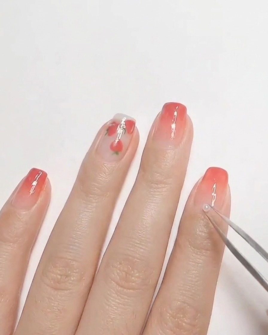 A pair of tweezers placing a small white pearl onto uncured hard gel on a fingernail.