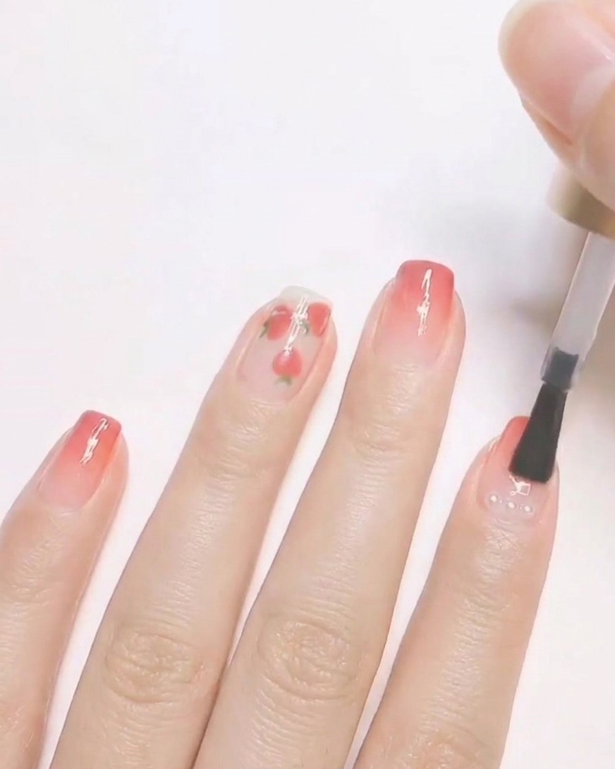 A nail brush applying clear top coat over a finished nail design featuring small encapsulated pearls.