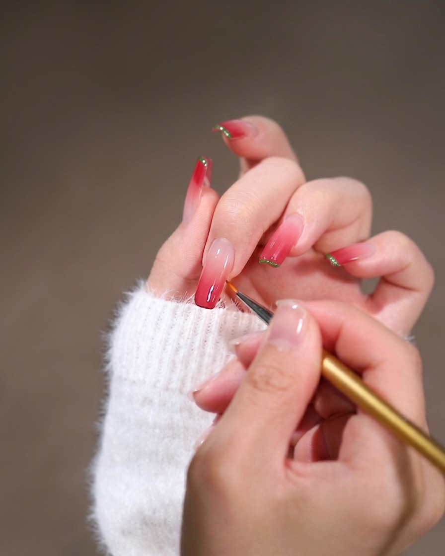 A close-up of a fine liner brush blending pink gel polish along the cuticle edge of a long square nail.