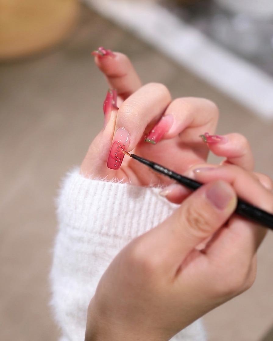 A detail shot of a fine tool placing a tiny gold stud onto the wet gel near the nail base.