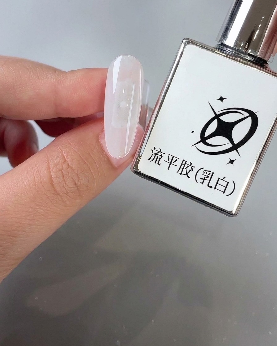 A brush applying milky white self-leveling gel onto an almond-shaped nail surface next to its product bottle.