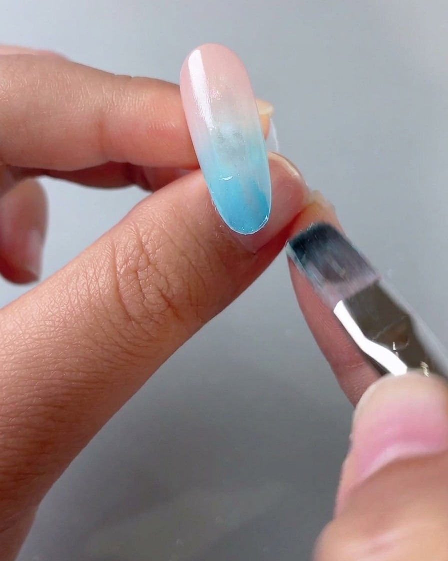 A brush applying a second layer of blue glass gel to the front half of the nail tip.